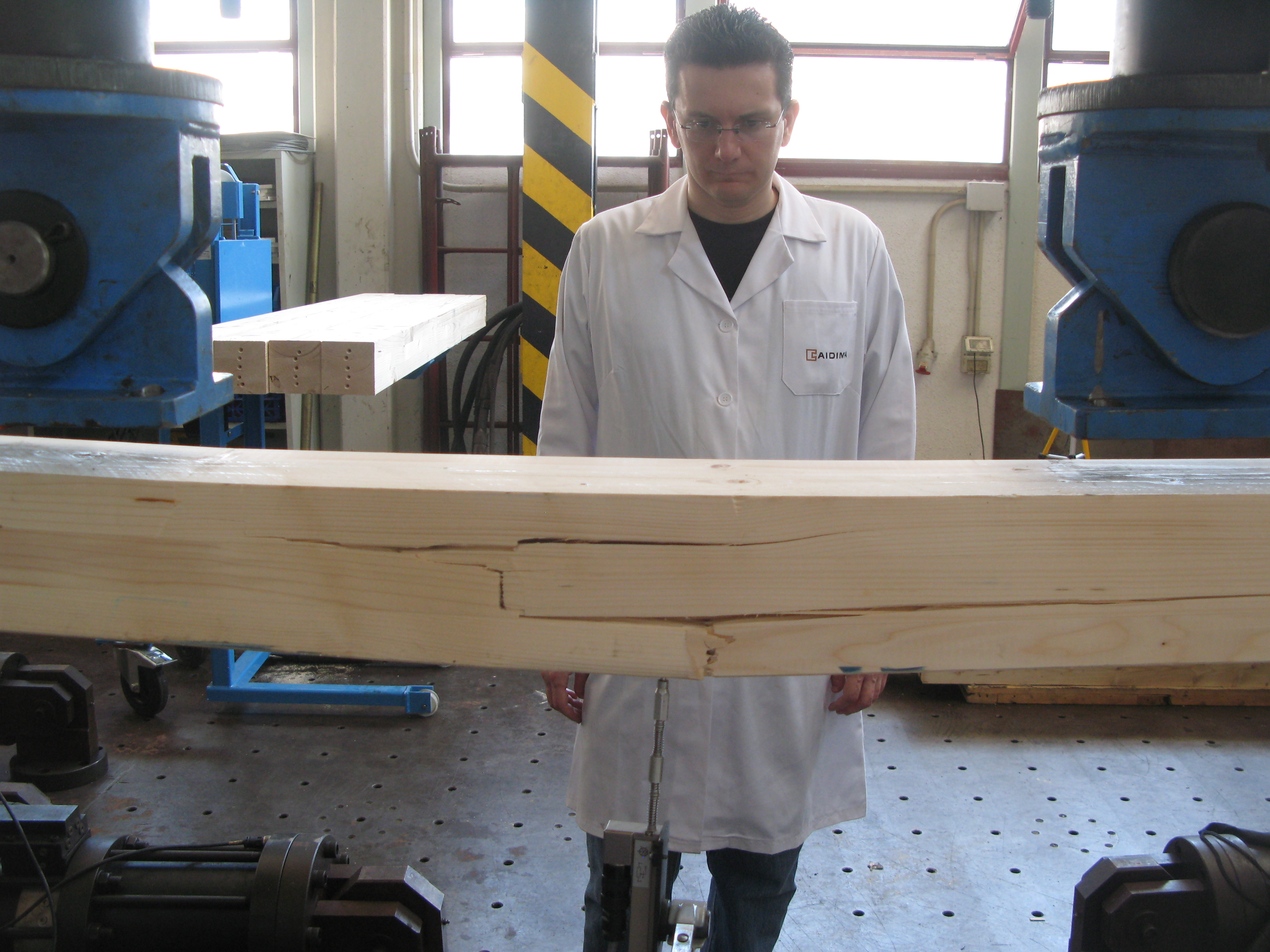Fotografía 3. Rotura de una viga de madera en un ensayo a flexión según la norma UNE-EN 408, mediante máquina universal de ensayos. Muy rara vez pueden realizarse estos ensayos destructivos en madera antigua y patrimonial; y para madera nueva tienen un coste muy elevado y se desaprovecha material.