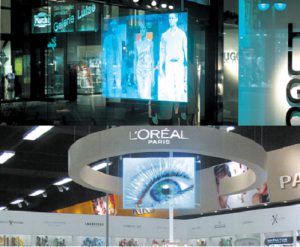 Ejemplos de una de las tecnologías multimedia analizadas para el proyecto (pantallas holográficas). Estas pantallas son proyecciones holográficas que muestran imágenes proyectadas hacia atrás de 30 a 35º. El resto de la luz no se considera, lo que genera imágenes muy brillantes y contrastadas, incluso en entornos muy iluminados. Estas pantallas permiten a los espectadores ver a través de ellas, y dan la sensación de estar suspendidas en el aire y de tener una profundidad 3D. Fuentes: Hugo Boss y L’Oréal Paris